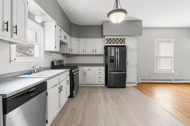 a kitchen with stainless steel appliances granite countertop a refrigerator a stove a sink and white cabinets with wooden floor