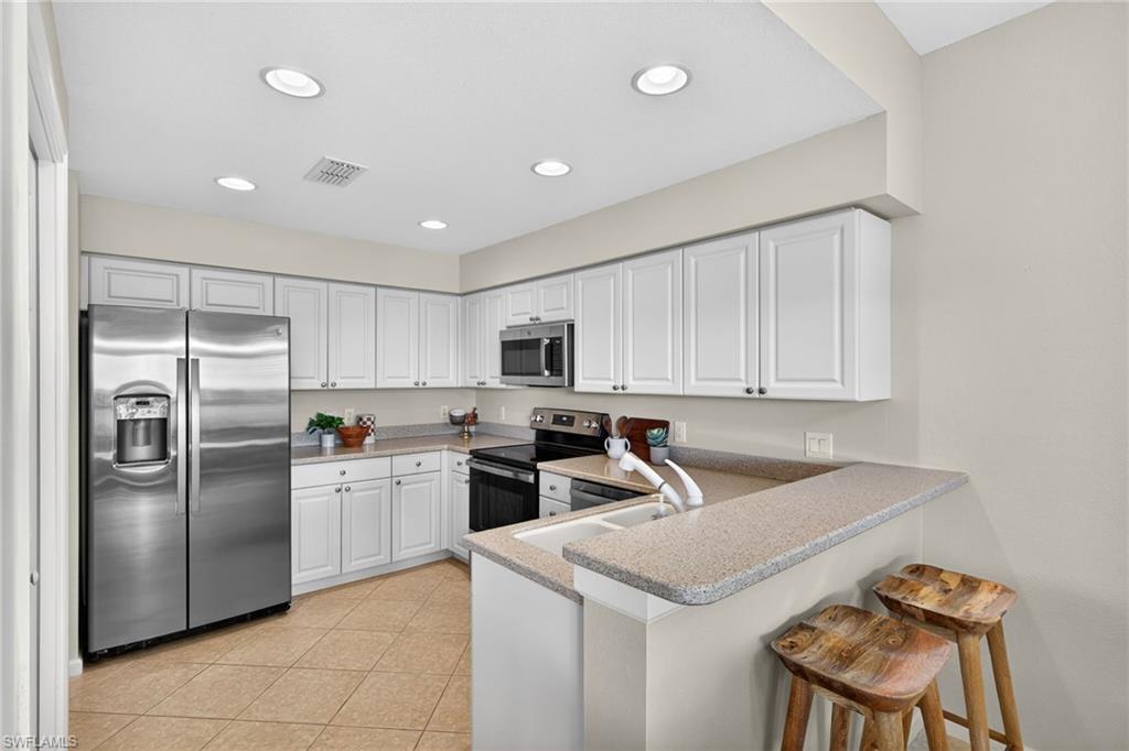 9201 Palmetto Ridge Drive, Unit 101 Estero, FL 34135 - Photo 8 of 29 Kitchen with a peninsula, stainless steel appliances, white cabinets, a breakfast bar, and recessed lighting