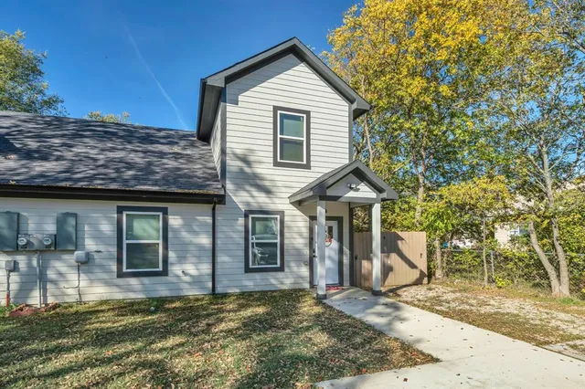 a view of a house with a small yard and large tree