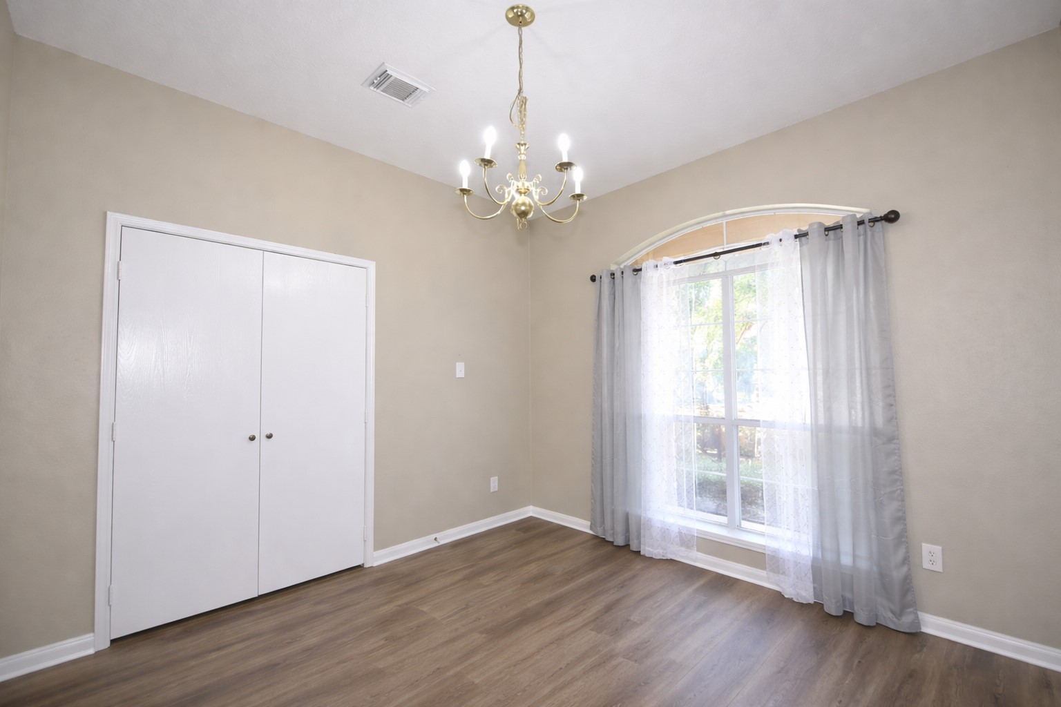 9611 Babbling Spring Court Tomball, TX 77375 - Photo 6 of 31 This room features a large window with sheer curtains, allowing natural light to flow in. It has neutral walls, a closet with white doors, and a central chandelier, complemented by wood flooring. Perfect for a bedroom or office space.