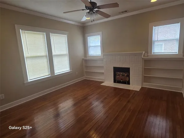 a view of an empty room with wooden floor fireplace and a window