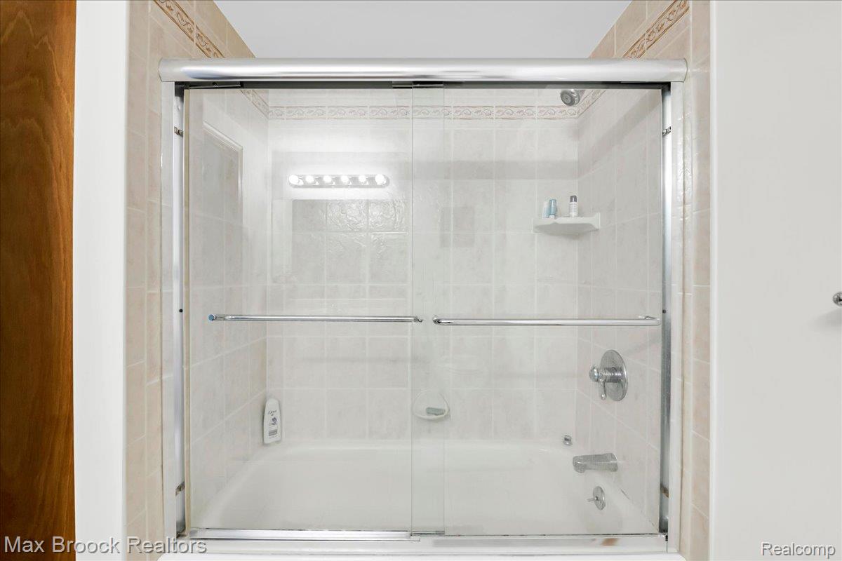 217 Stonetree Circle Rochester, MI 48309 - Photo 39 of 44 Bathtub with sliding glass shower doors, chrome fixtures, and a tiled surround with decorative accent border