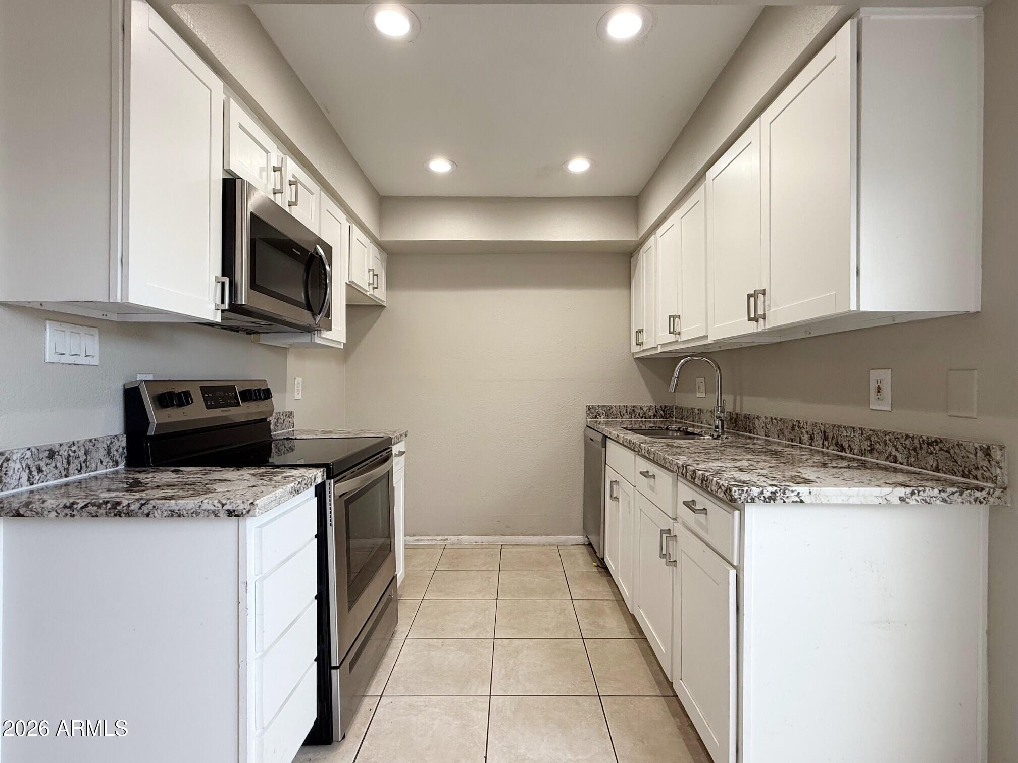 3840 North 43rd Avenue, Unit 34 Phoenix, AZ 85031 - Photo 5 of 18 a kitchen with stainless steel appliances granite countertop a stove top oven a sink a microwave and a refrigerator