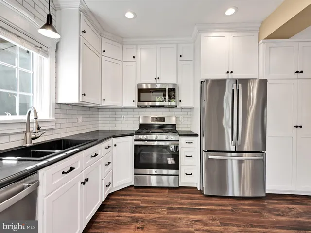a kitchen with granite countertop a refrigerator stove and white cabinets