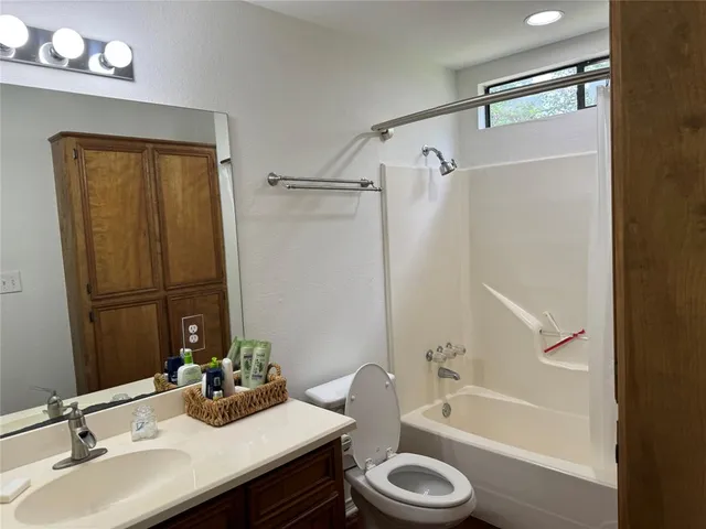 a bathroom with a granite countertop bathtub shower sink vanity and toilet