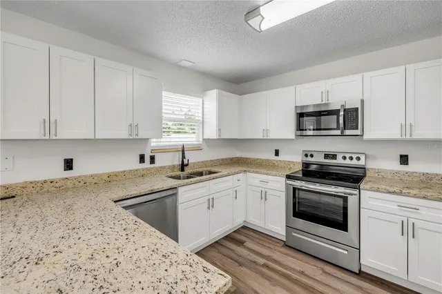 a kitchen with granite countertop white cabinets sink and stainless steel appliances