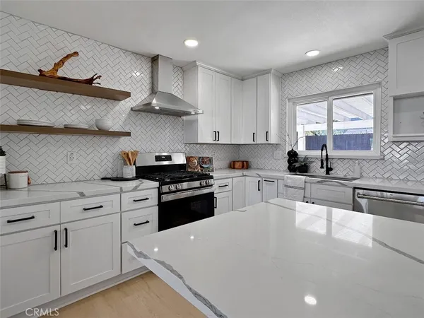 a white kitchen with stainless steel appliances granite countertop a stove a sink a refrigerator and white cabinets