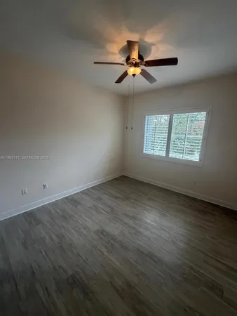 an empty room with wooden floor chandelier fan and windows