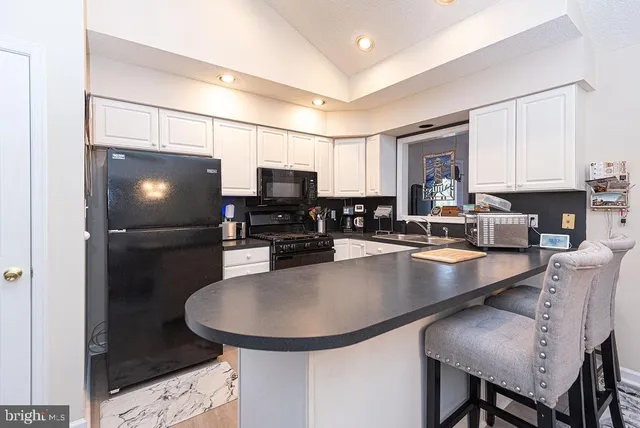 a kitchen with stainless steel appliances granite countertop a sink a stove a microwave a refrigerator a stove and white cabinets with wooden floor