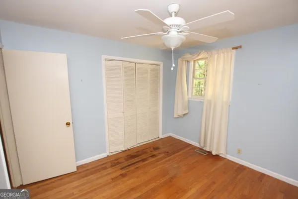 a view of an empty room with wooden floor and a ceiling fan