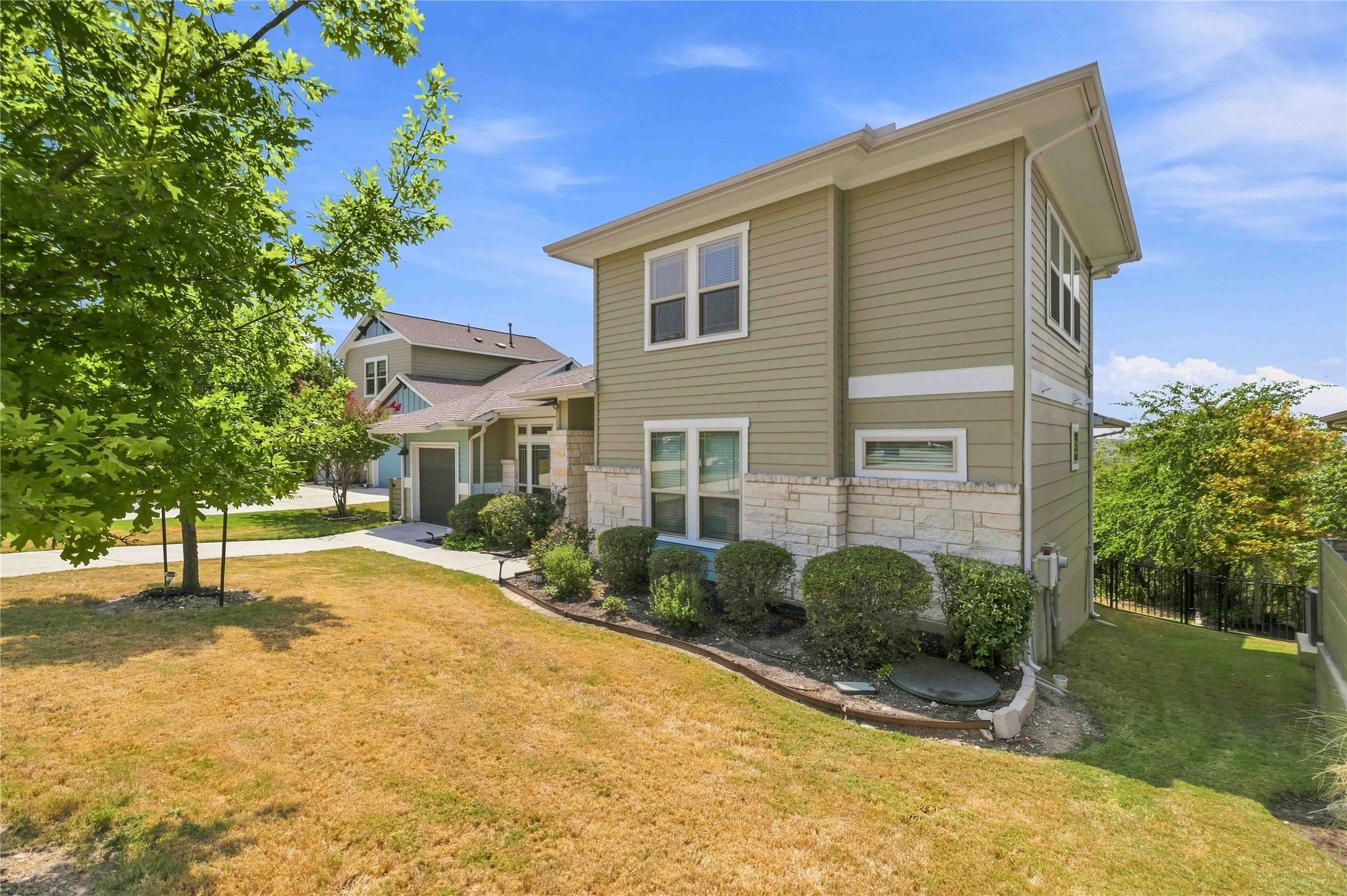 Charming two-story home with a modern exterior, featuring a mix of light green siding and stone accents. The well-maintained lawn and landscaping add to the curb appeal, while the surrounding trees provide a touch of nature.