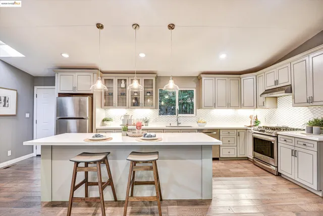 a kitchen with stainless steel appliances kitchen island granite countertop a stove a sink a refrigerator white cabinets and wooden floor