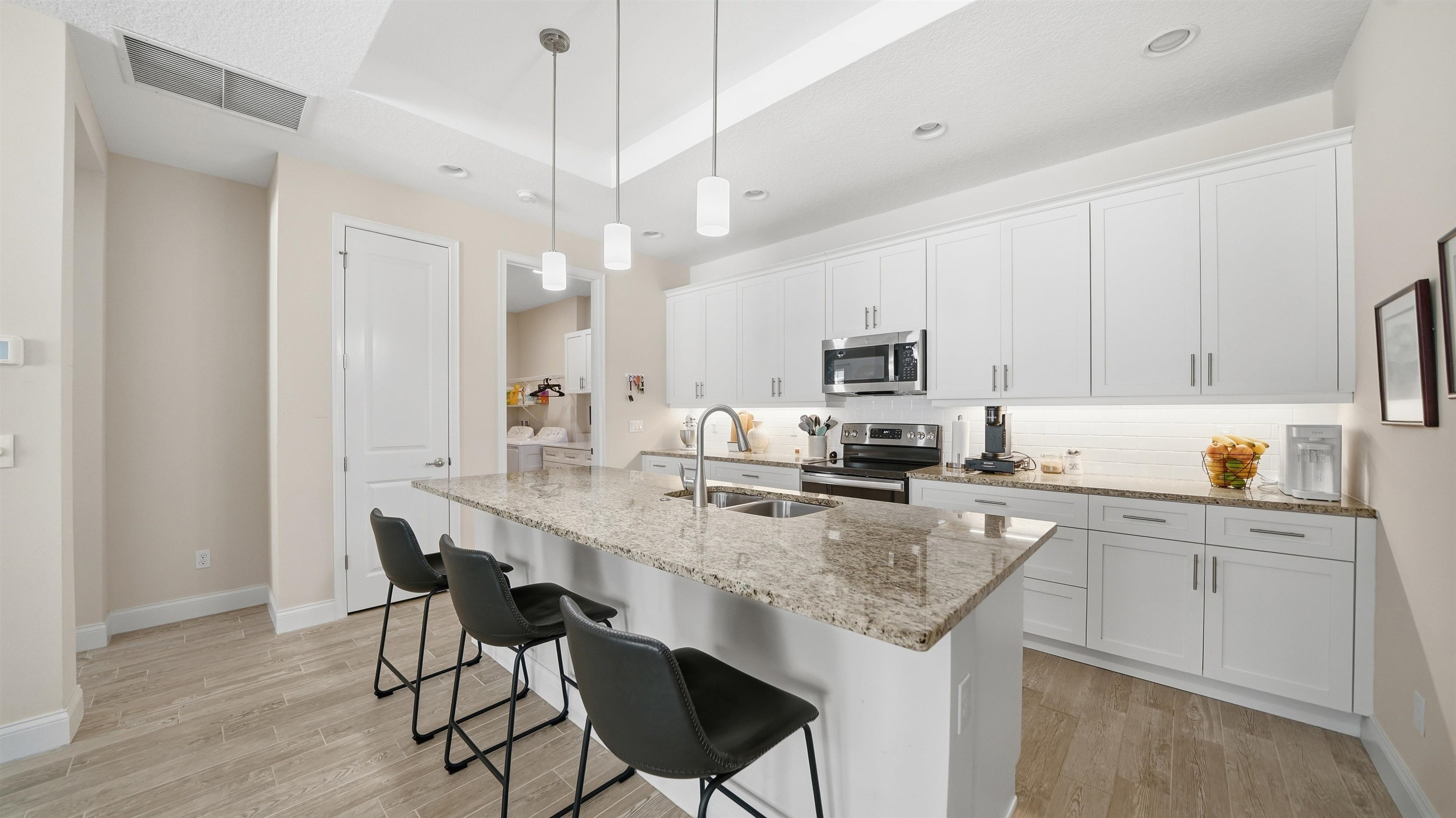 74 Wrendale Loop Ormond Beach, FL 32174 - Photo 8 of 59 Kitchen with white cabinetry, light wood-style floors, light stone counters, a kitchen bar, and stainless steel appliances