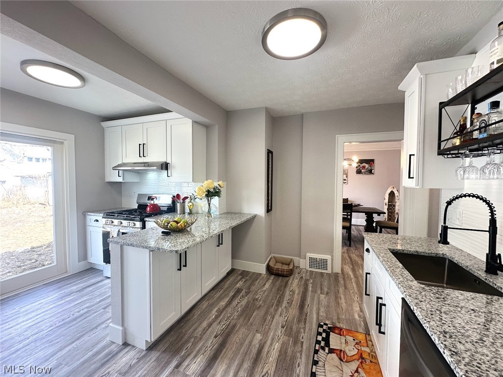 Kitchen featuring white cabinets, decorative backsplash, light stone countertops, gas range, and dark wood-style floors