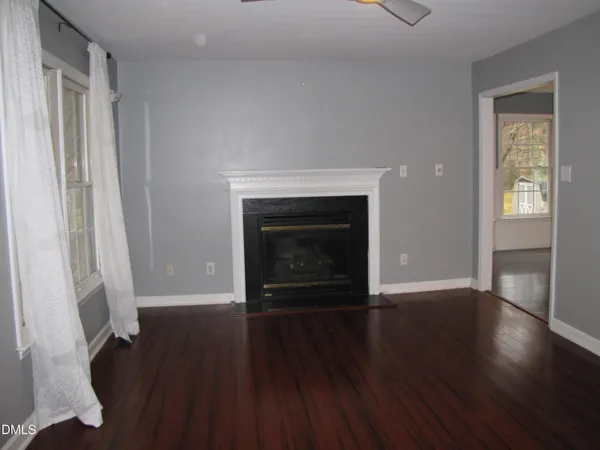 an empty room with wooden floor fireplace and windows