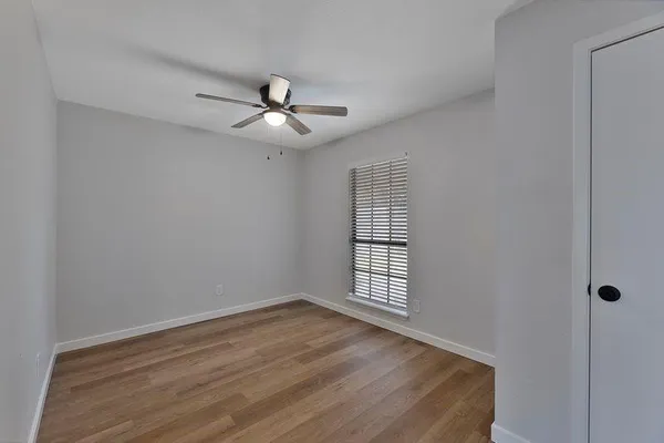 an empty room with wooden floor ceiling fan and windows