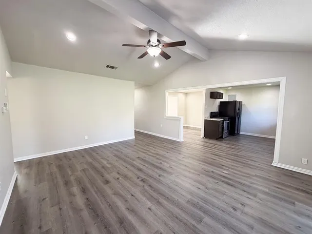 a view of an empty room with wooden floor and a ceiling fan