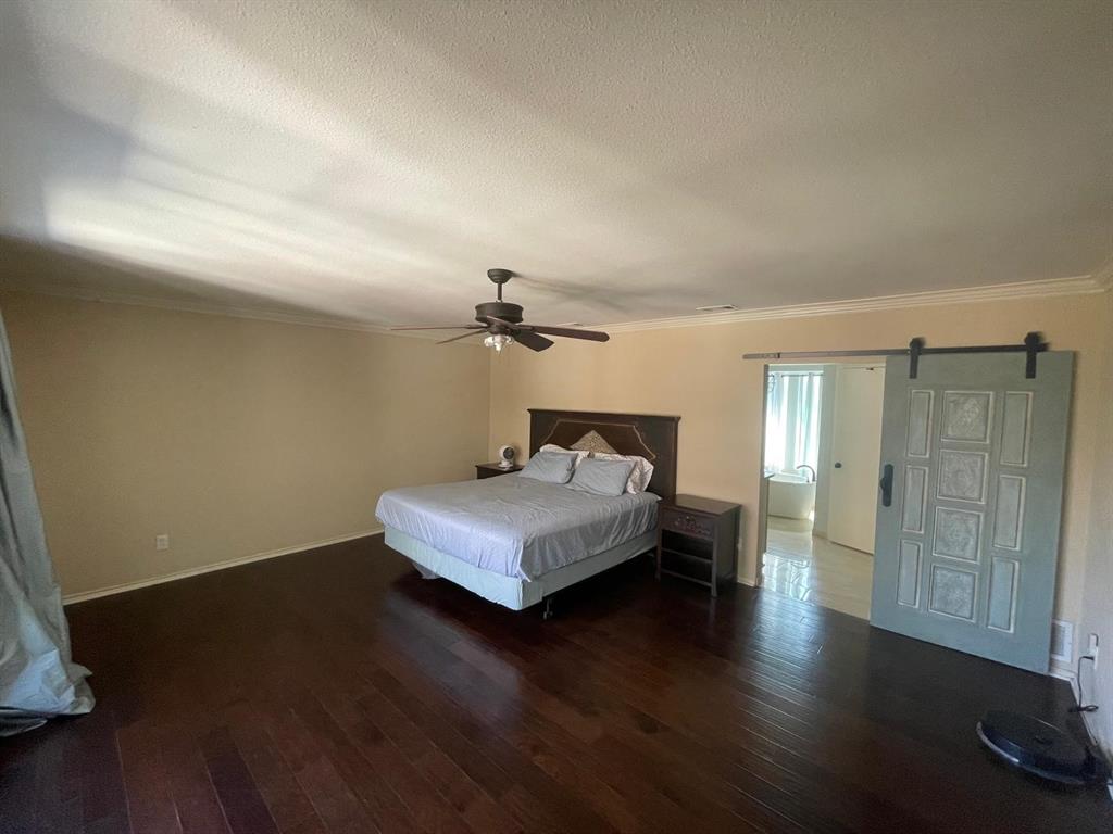 3612 Cross Bend Road Plano, TX 75023 - Photo 24 of 38 Unfurnished bedroom featuring ceiling fan, a barn door, ornamental molding, wood-type flooring, and a textured ceiling