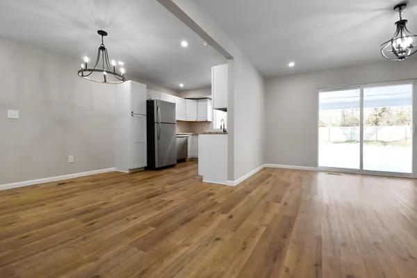 an empty room with wooden floor kitchen appliances and windows