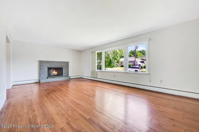 a view of an empty room with wooden floor fireplace and a window