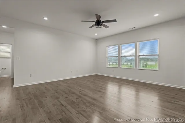 an empty room with wooden floor chandelier fan and windows
