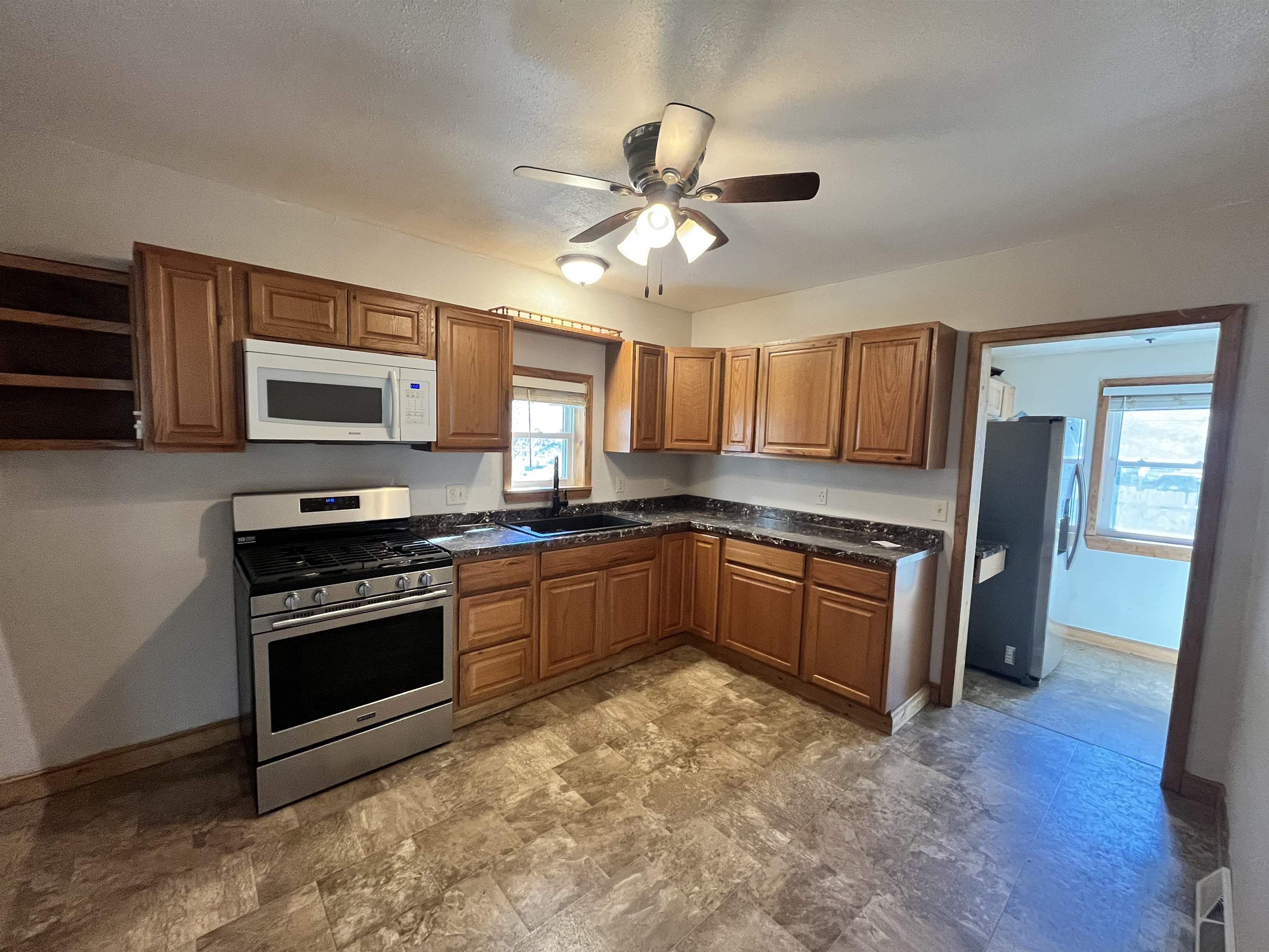 14 3rd Street Proctor, MN 55810 - Photo 6 of 19 Kitchen featuring brown cabinetry, stainless steel appliances, ceiling fan, stone finish floors, and open shelves