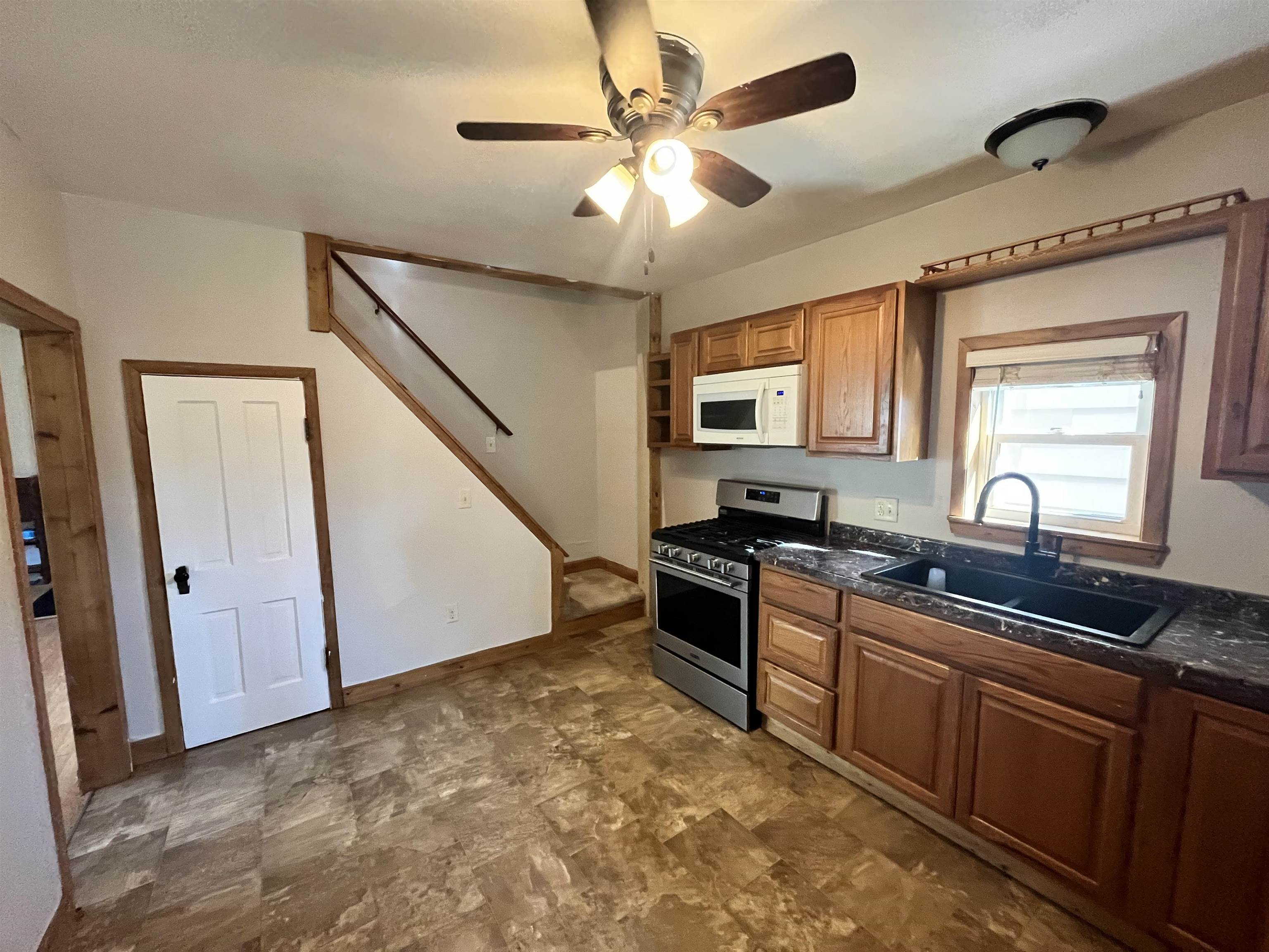 14 3rd Street Proctor, MN 55810 - Photo 7 of 19 Kitchen featuring stainless steel gas range, brown cabinets, white microwave, a ceiling fan, and stone finish flooring