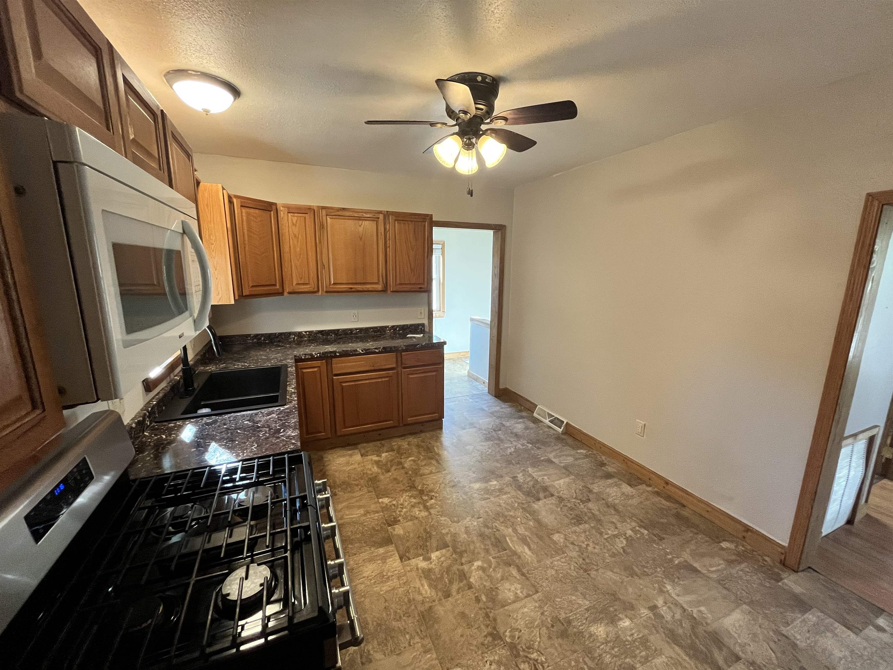 14 3rd Street Proctor, MN 55810 - Photo 8 of 19 Kitchen with stainless steel range with gas cooktop, white microwave, brown cabinets, stone finish floors, and ceiling fan