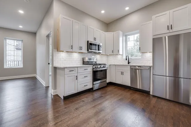 a kitchen with stainless steel appliances granite countertop a refrigerator a sink dishwasher a stove and white countertops with wooden floor