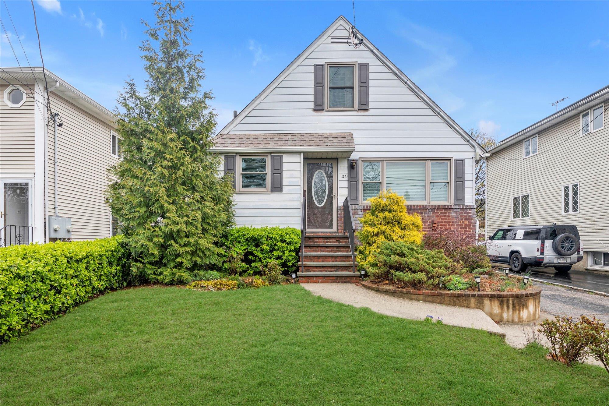 36 Graywood Road Port Washington, NY 11050 - Photo 1 of 1 Cape-style house featuring brick siding, a shingled roof, entry steps, and a front lawn