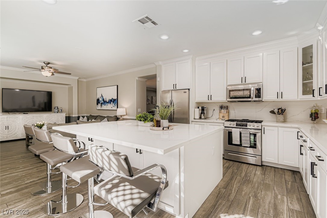 7055 Fort Tule Avenue Las Vegas, NV 89179 - Photo 2 of 75 Kitchen with a center island, stainless steel appliances, white cabinetry, a breakfast bar, and decorative backsplash