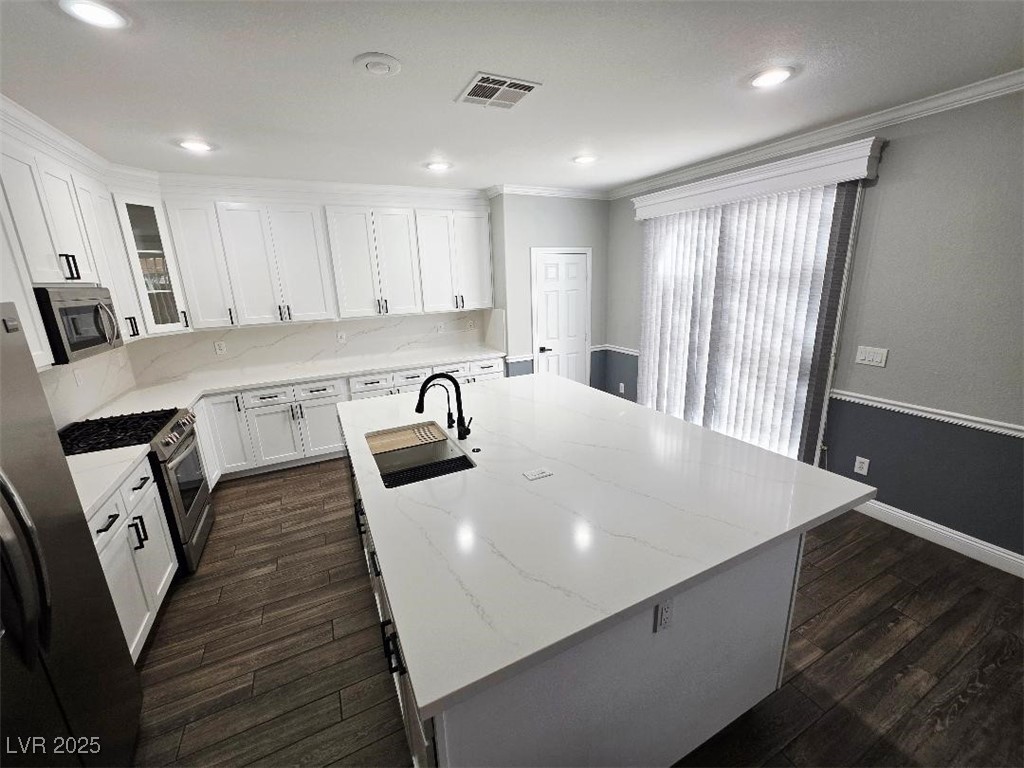 7055 Fort Tule Avenue Las Vegas, NV 89179 - Photo 10 of 75 Kitchen featuring a center island with sink, decorative backsplash, appliances with stainless steel finishes, light stone counters, and white cabinetry