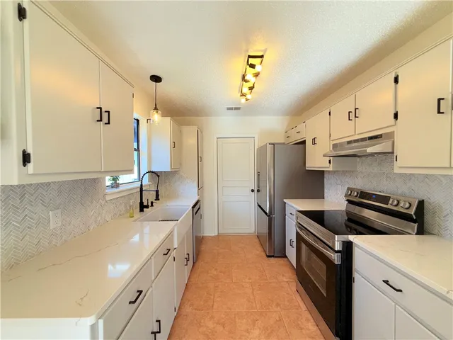 a large kitchen with stainless steel appliances a sink a stove and a refrigerator