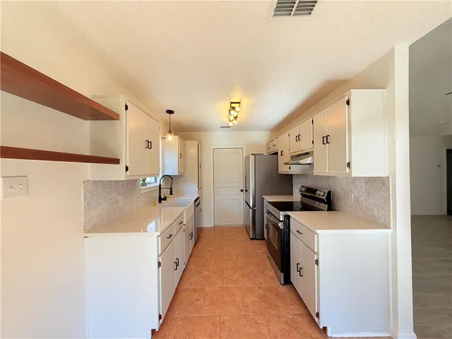 a large white kitchen with stainless steel appliances a refrigerator a stove top oven a sink and dishwasher