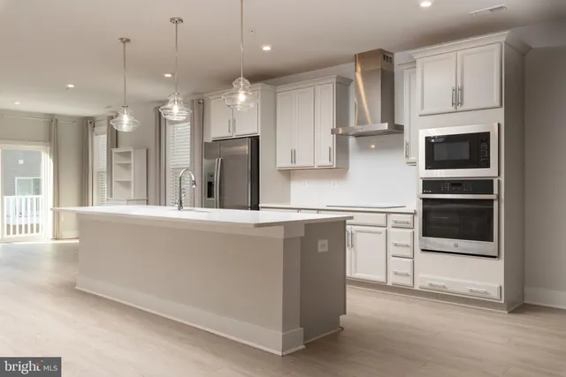 a kitchen with stainless steel appliances kitchen island granite countertop a refrigerator a sink a stove and white cabinets with wooden floor