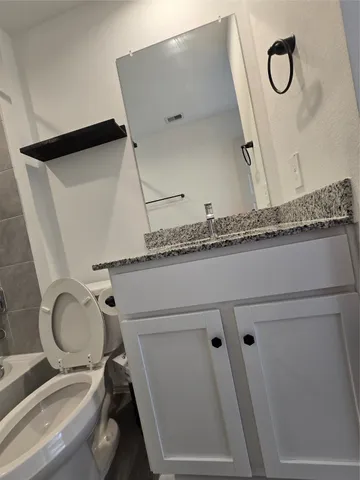 a bathroom with a granite countertop sink a toilet and a mirror