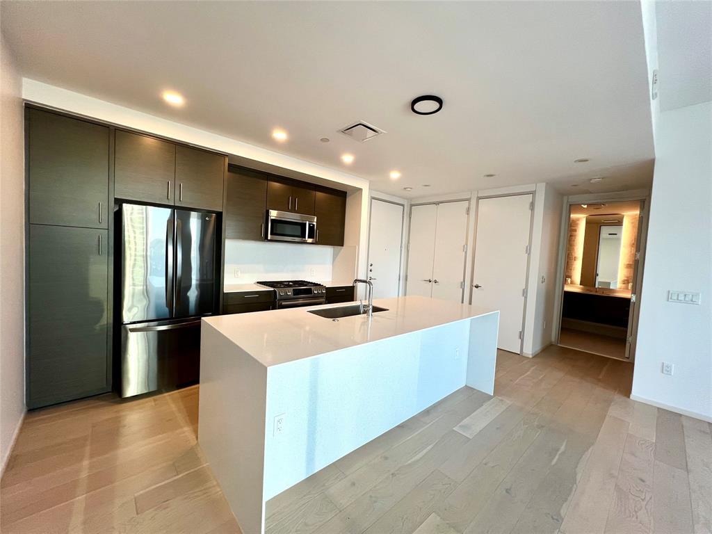 301 West Avenue, Unit 1502 Austin, TX 78701 - Photo 2 of 26 Kitchen with stainless steel appliances, modern cabinets, light wood-style flooring, light stone counters, and an island with sink