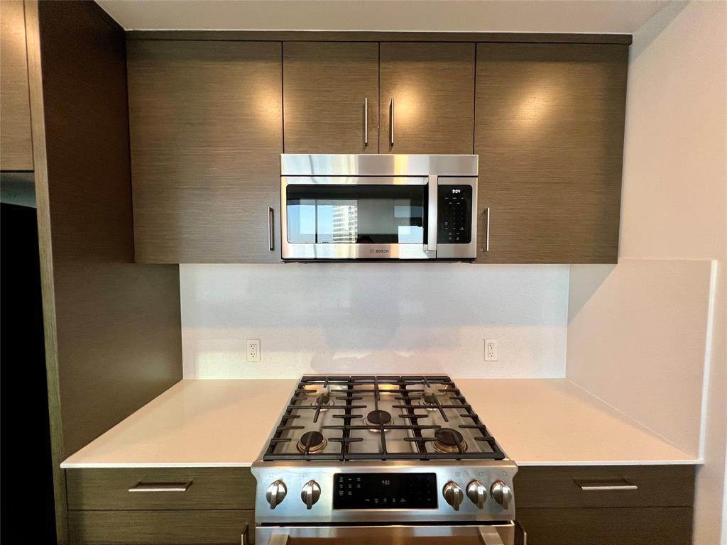 301 West Avenue, Unit 1502 Austin, TX 78701 - Photo 5 of 26 Kitchen with appliances with stainless steel finishes, modern cabinets, dark brown cabinets, and light stone countertops