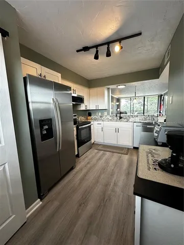 a kitchen with stainless steel appliances granite countertop a refrigerator a sink dishwasher a stove and white countertops with wooden floor