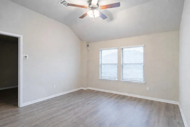 an empty room with wooden floor chandelier fan and windows