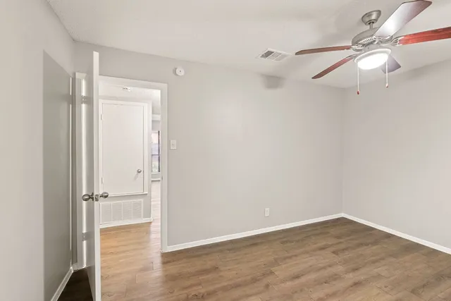 a view of an empty room with wooden floor and a ceiling fan