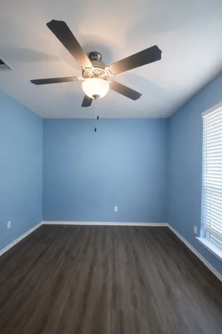 an empty room with wooden floor fan and windows