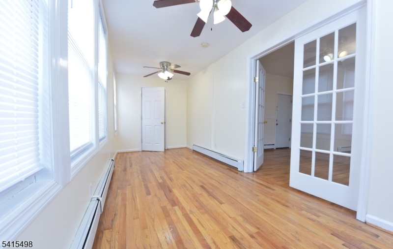 117 Scheerer Avenue Newark, NJ 07112 - Photo 13 of 19 an empty room with wooden floor fan and windows