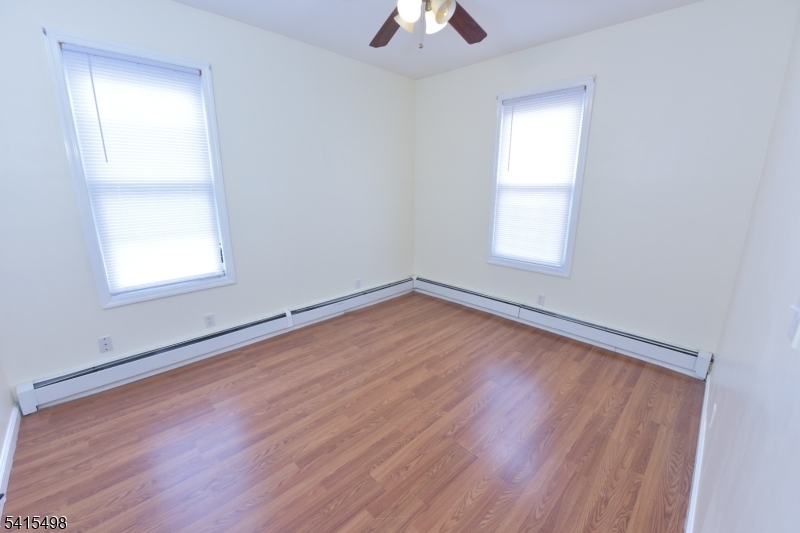 117 Scheerer Avenue Newark, NJ 07112 - Photo 5 of 19 an empty room with wooden floor chandelier fan and windows