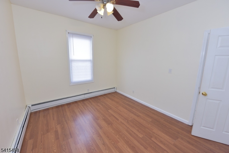 117 Scheerer Avenue Newark, NJ 07112 - Photo 9 of 19 an empty room with wooden floor chandelier fan and windows