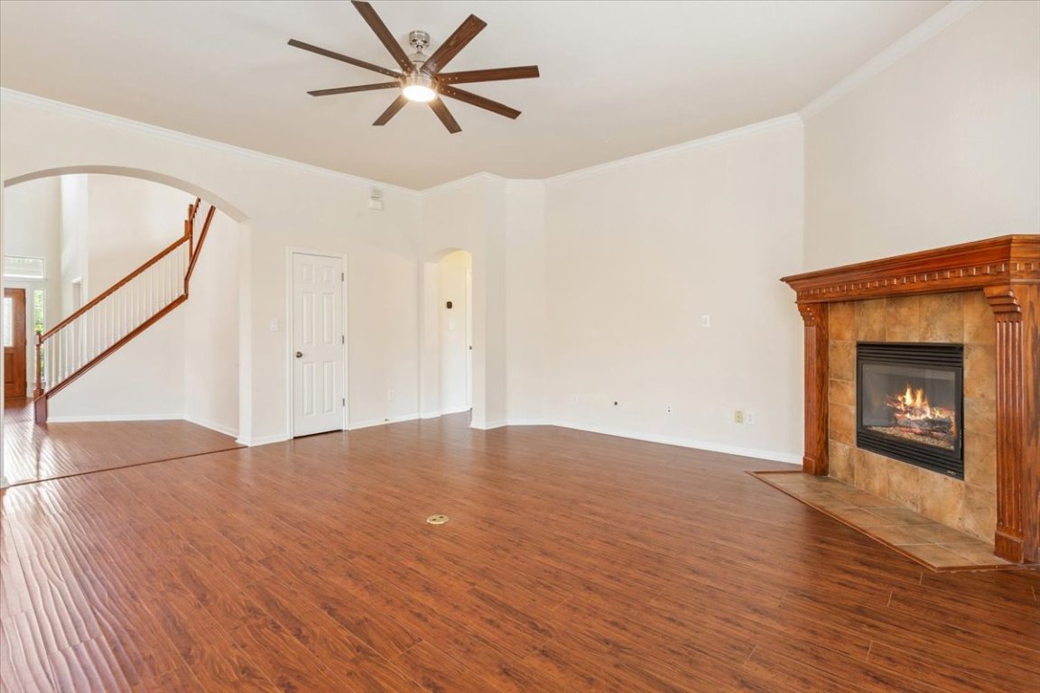 102 Country View Way Cedar Park, TX 78613 - Photo 13 of 38 Unfurnished living room with ceiling fan, a tiled fireplace, arched walkways, crown molding, and wood finished floors
