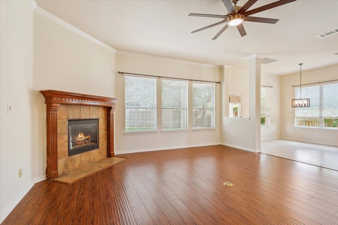 102 Country View Way Cedar Park, TX 78613 - Photo 15 of 38 Unfurnished living room featuring a fireplace, a ceiling fan, wood finished floors, ornamental molding, and a chandelier