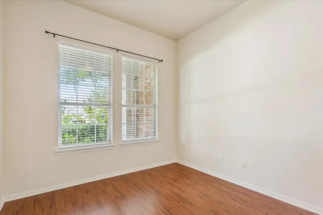 an empty room with wooden floor fan and windows