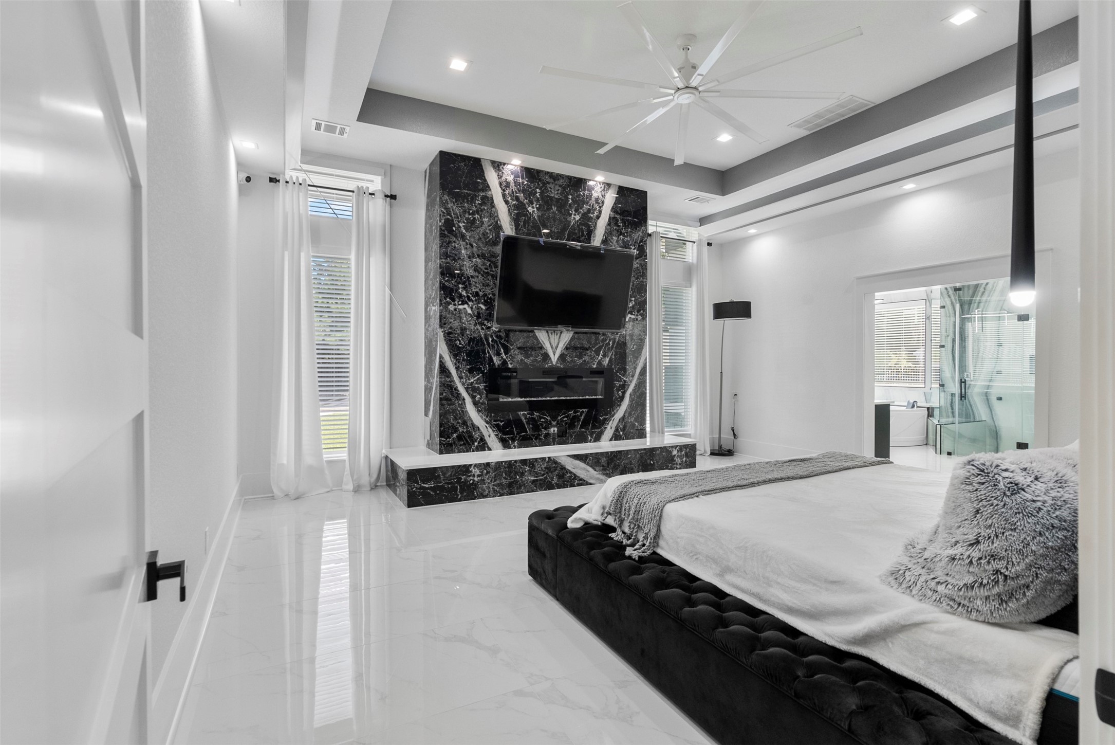 12 County Road 3558 Cleveland, TX 77327 - Photo 12 of 50 Luxurious primary bedroom featuring a striking real stone accent wall with quartz detailing below and a sleek built-in fireplace, creating an elegant and upscale retreat.