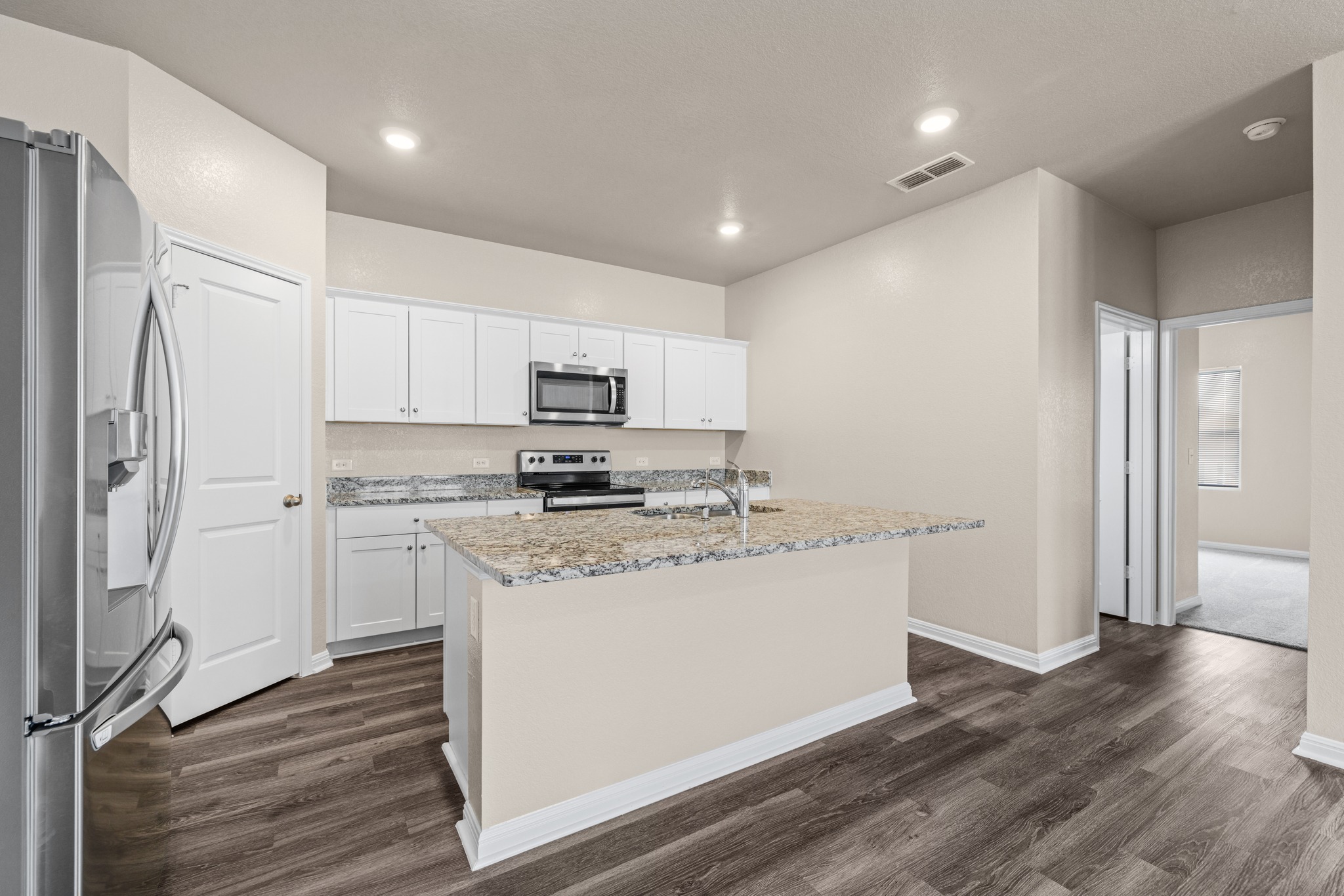 241 Night Riders Way Jarrell, TX 76537 - Photo 11 of 39 Kitchen featuring stainless steel appliances, white cabinetry, an island with sink, dark wood-type flooring, and light stone counters
